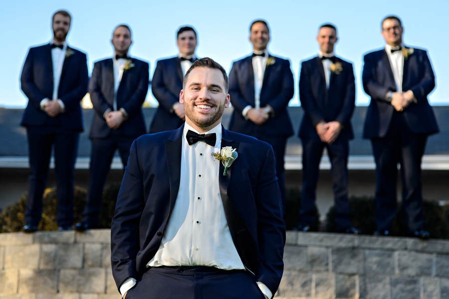 A portrait of a groom with his groomsmen in the background.